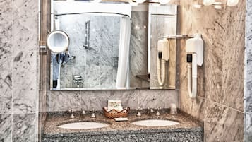 Un bagno con pareti in marmo, un ampio specchio, due lavabi e un portascopino.