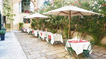 Un patio al aire libre con mesas y sillas, cubierto por sombrillas, rodeado de vegetación.