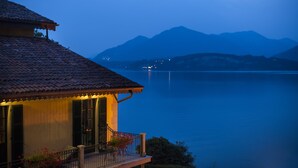 Una casa con techo de tejas que domina un lago tranquilo y montañas a lo lejos.