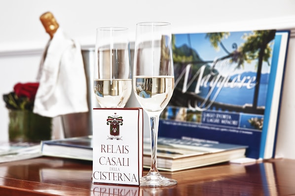 Dos copas de vino blanco sobre una mesa de madera con una tarjeta de menú que dice "RELAIS CASALI DELLA CISTERNA" y un libro con una imagen de la costa al fondo.