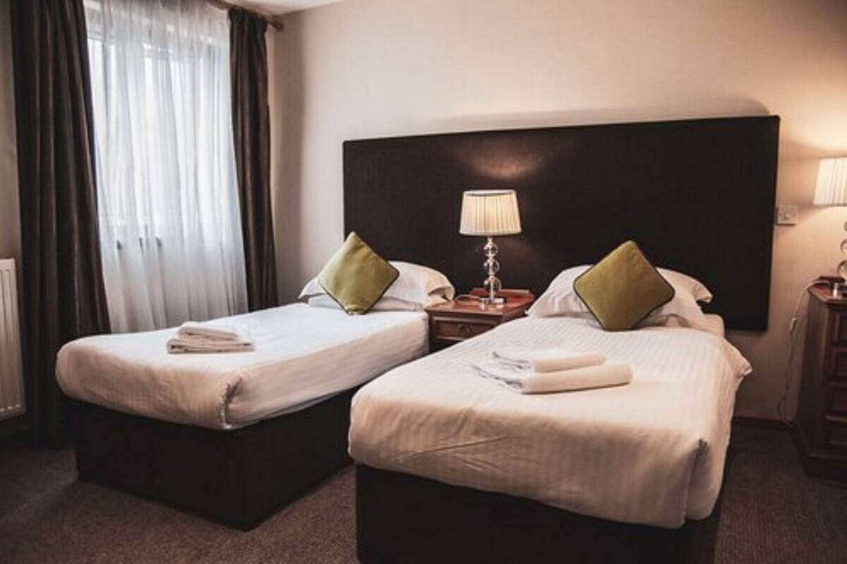 A hotel room with two single beds, a dark headboard, bedside lamps, and a window with curtains.