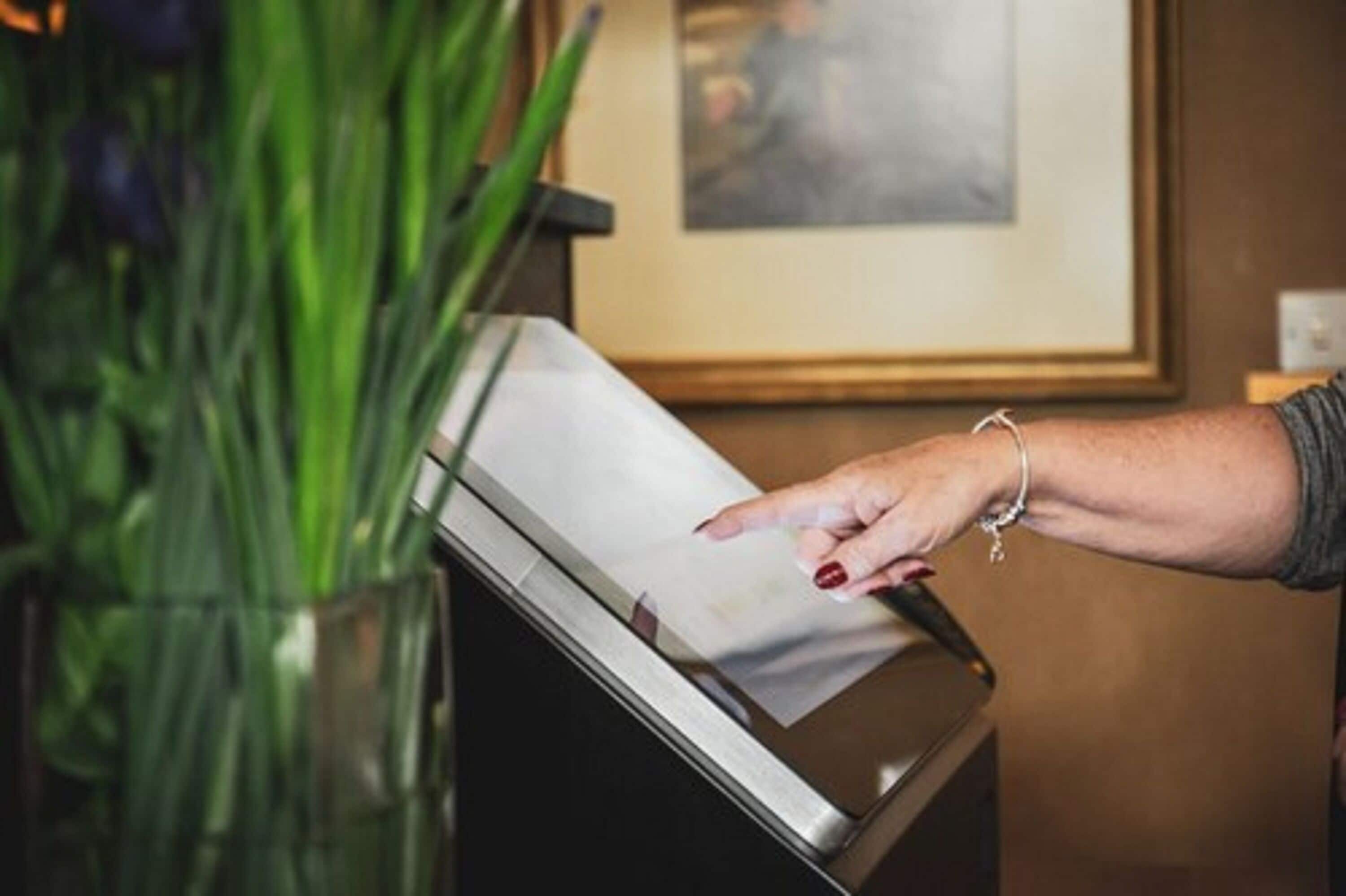 A hand interacting with a touch screen kiosk, likely for check-in or information purposes.