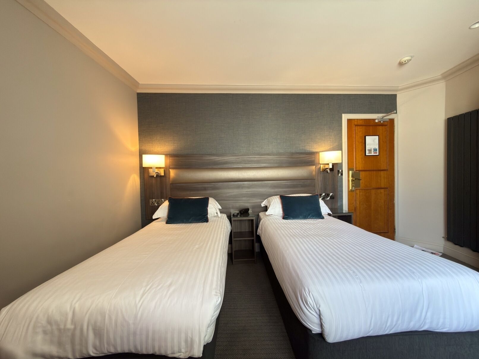 Una habitación de hotel con dos camas individuales, una puerta de madera y un aplique fijado a la pared.