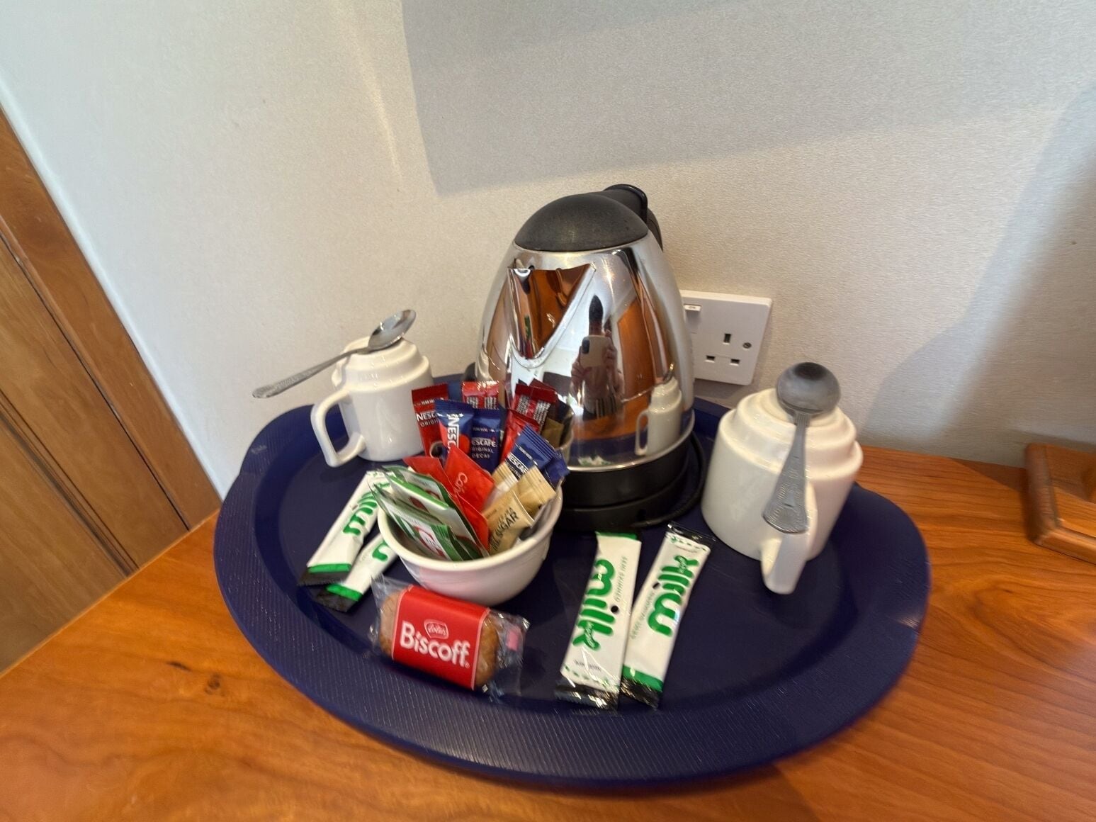 Una bandeja de desayuno con una cafetera, un tazón de cereal, una taza, una cuchara y varios paquetes de leche y galletas.