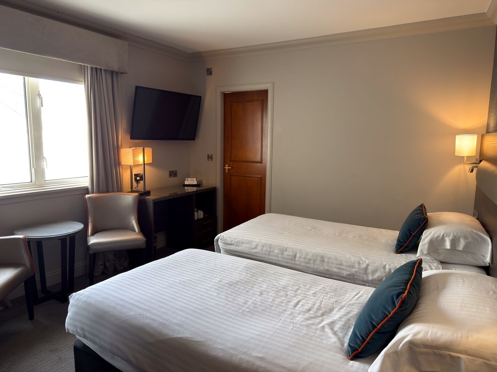 Une chambre d’hôtel avec deux lits, un bureau, une chaise, une télévision et une fenêtre.