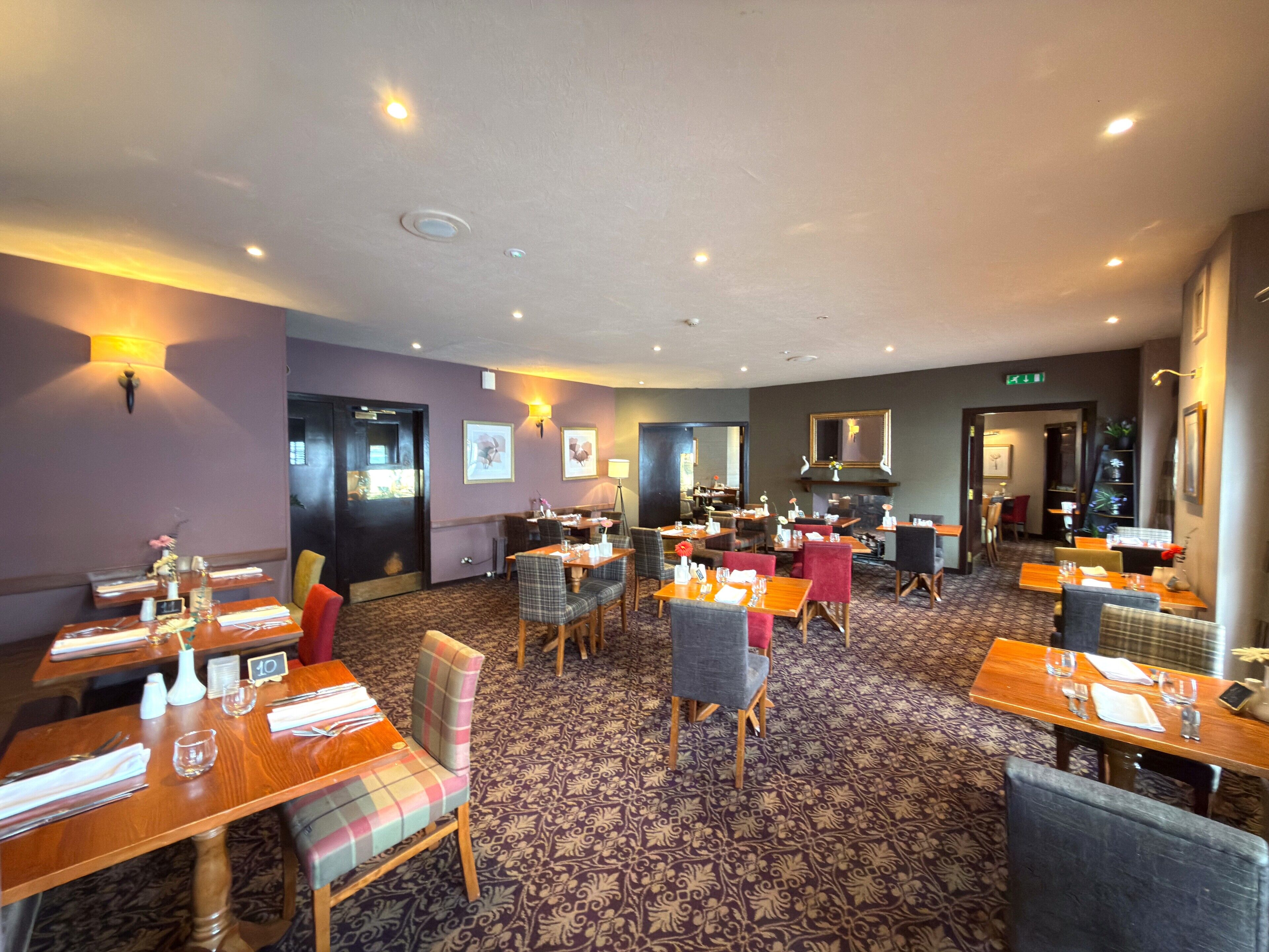 Une salle à manger d’hôtel avec plusieurs tables et chaises, un tapis à motifs et des luminaires fixés au mur.