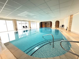 Uma piscina interior com água azul cristalina, chão em azulejo e teto com padrão quadriculado.