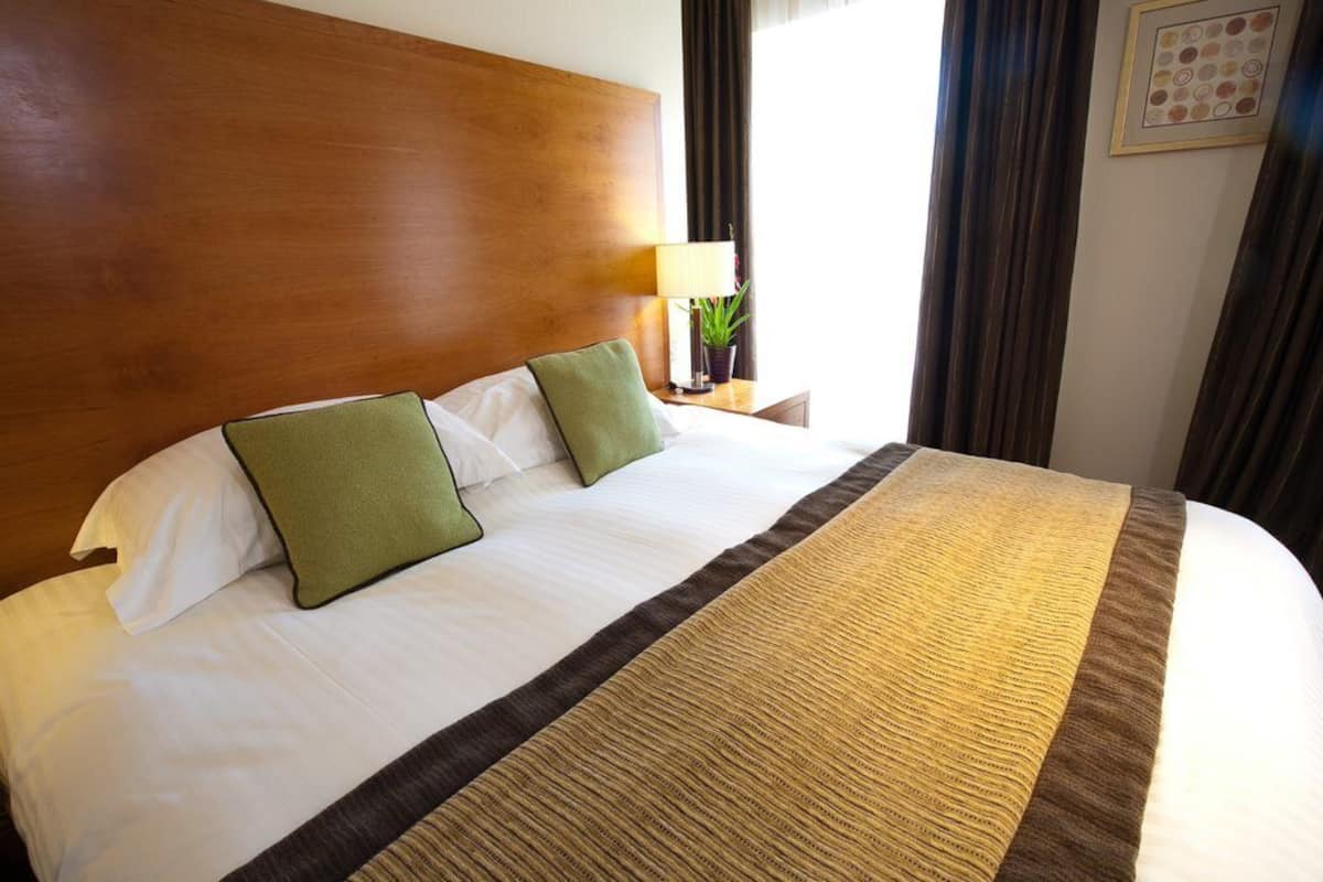 A neatly made bed with a wooden headboard, two pillows, a bedside lamp, and a framed picture on the wall.