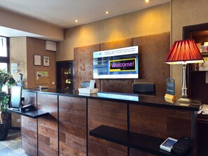 A hotel reception desk with a digital screen displaying a welcome message, a red lamp, and a sign indicating the hotel name.