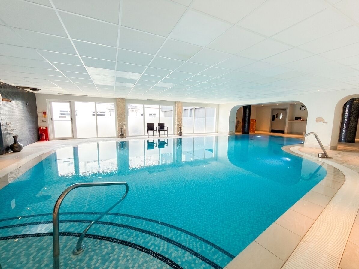Une piscine intérieure à l’eau claire, avec un escalier en métal et un sol carrelé.