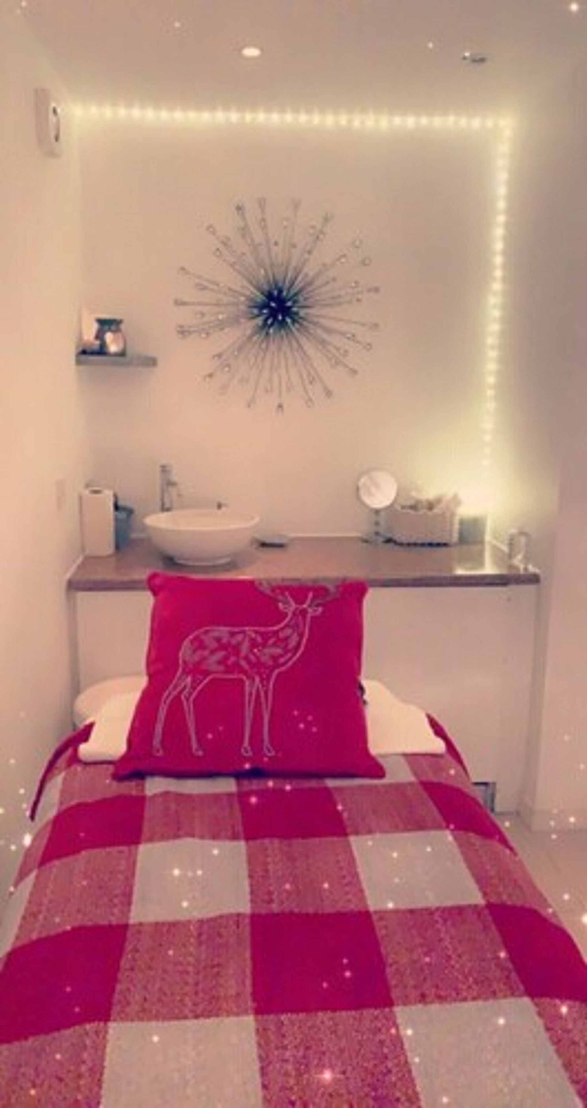Una camera da letto con una coperta a quadri, uno specchio fissato al muro e un lampadario decorativo.
