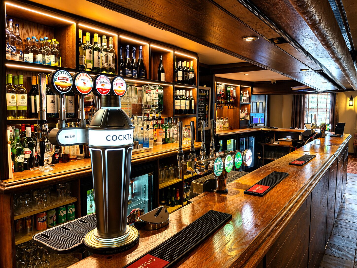 A bar area with a tap labeled 'COCKTAIL' and various bottles and glasses on shelves.