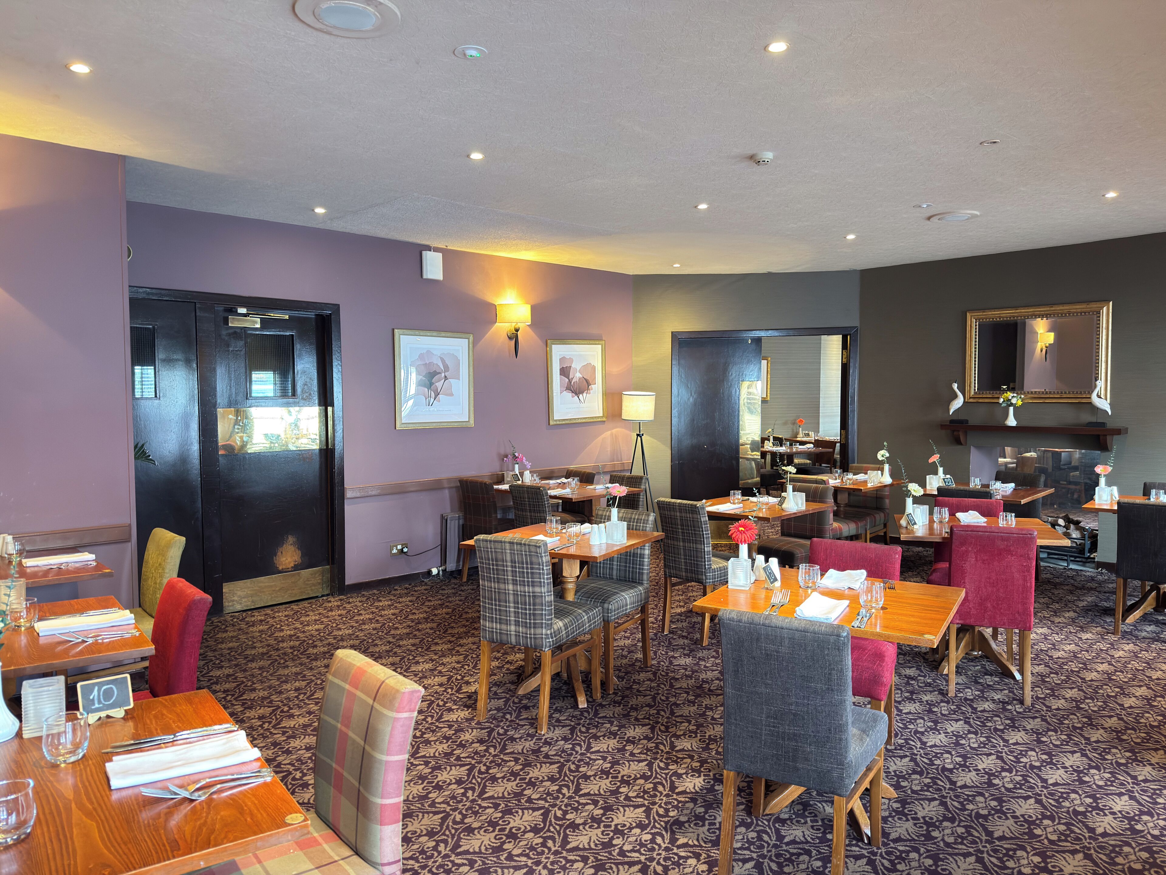 A hotel dining area with multiple tables and chairs, a fireplace, and wall-mounted artwork.