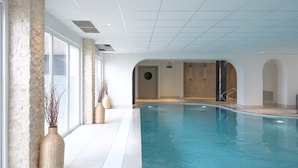Een binnenzwembad met glazen wanden, betegelde vloer en modern design, met een accentmuur van steen en een ronde deur.
