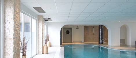 An indoor swimming pool with clear glass walls, a tiled floor, and a modern design with a stone accent wall and a circular door.