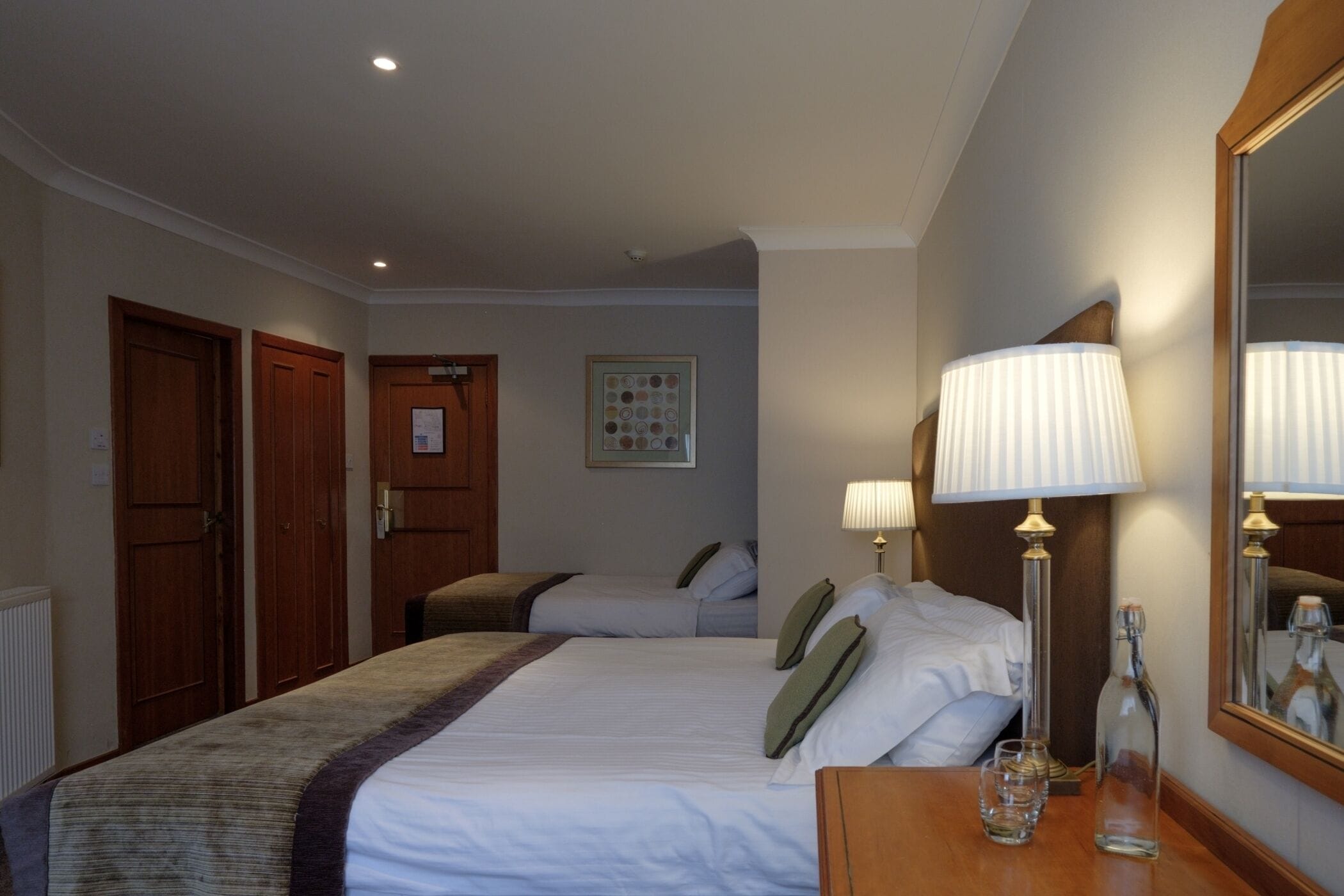 Habitación de hotel con dos camas, un aparador de madera, un espejo y un cuadro en la pared.