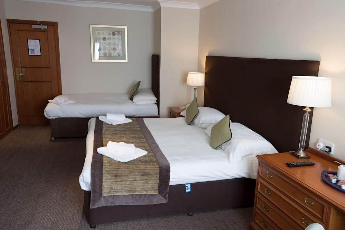 A hotel room with two beds, a wooden dresser, a lamp, and a framed picture on the wall.