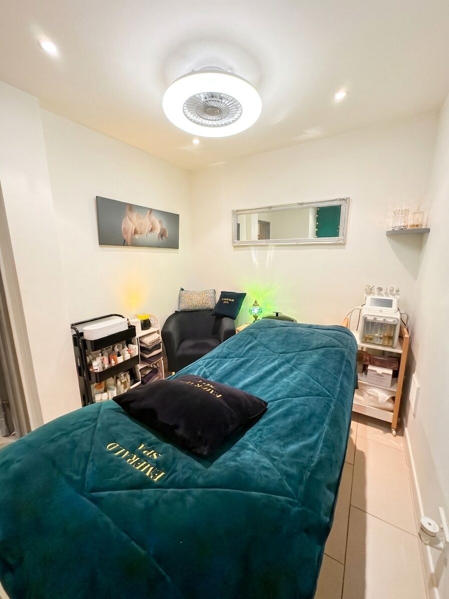 A room with a bed, a chair, a shelf with items, a mirror, and a ceiling light.
