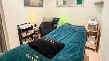 A room with a bed, a chair, a shelf with items, a mirror, and a ceiling light.