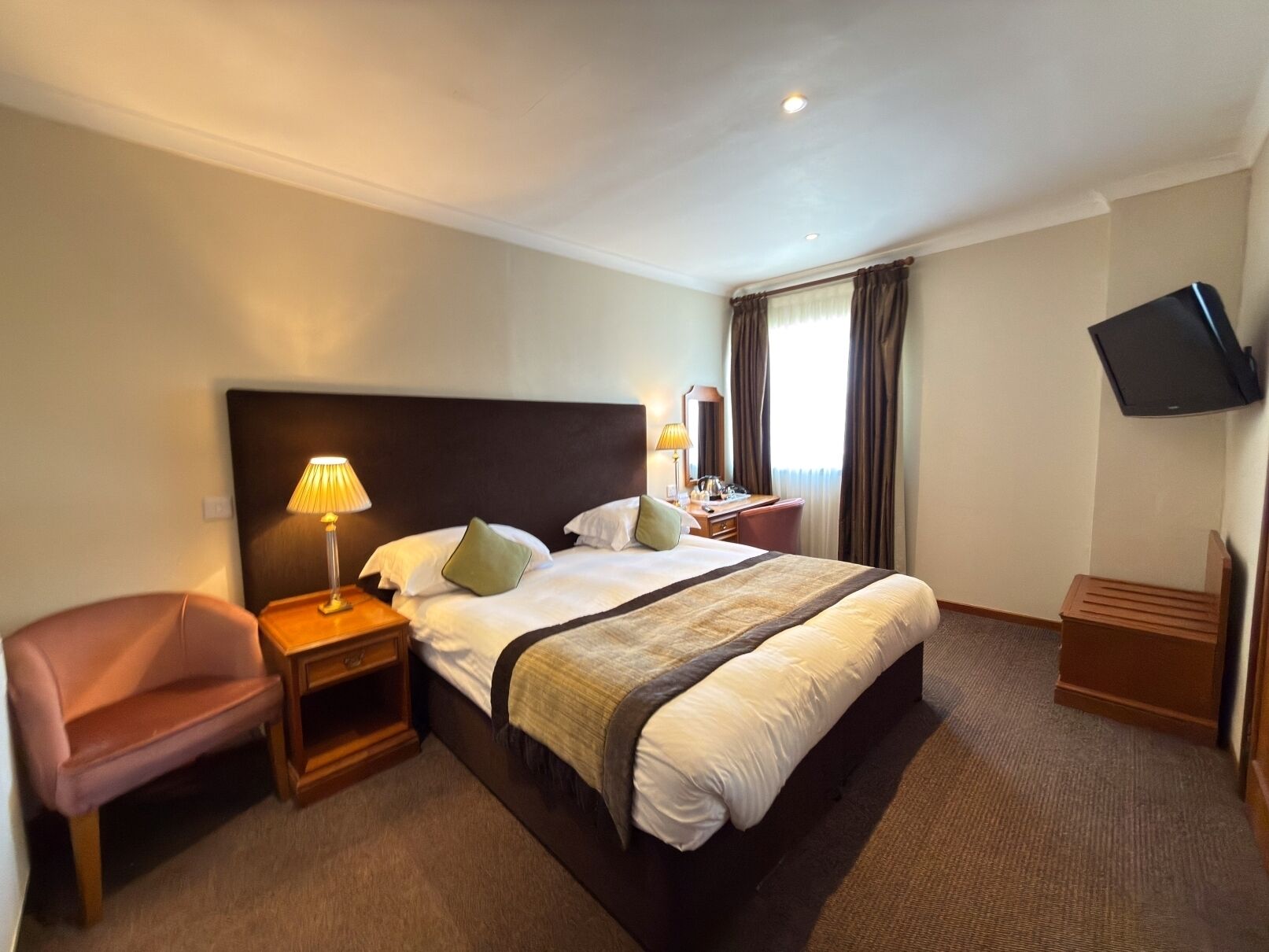 Una habitación de hotel con una cama grande, un escritorio con lámpara, una silla y un televisor montado en la pared.