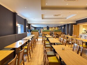 A spacious restaurant with multiple dining tables and chairs, a kitchen area, and a seating area with a view of the outdoors. - The Angus Hotel & Spa by Compass Hospitality (Blairgowrie)