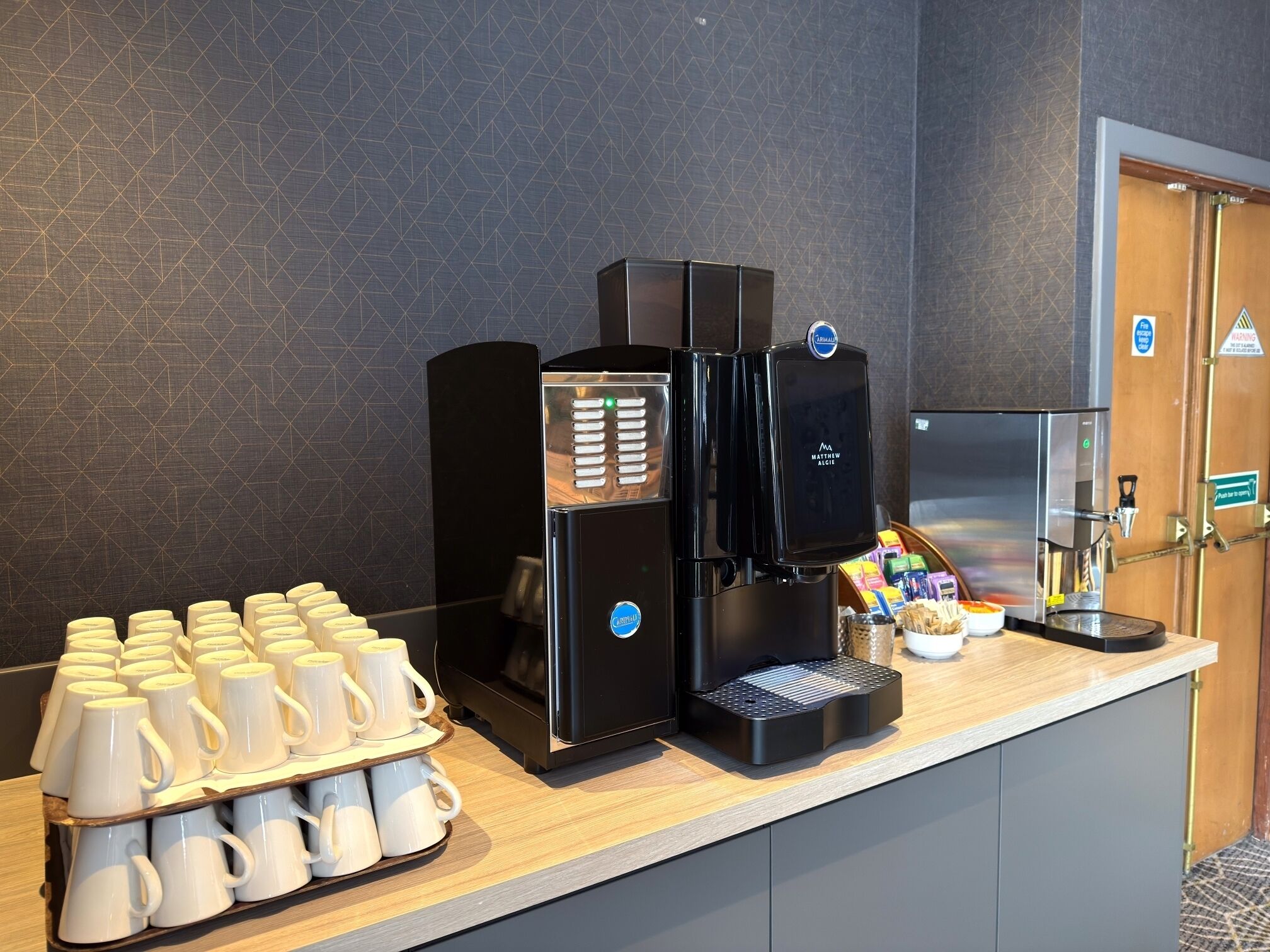 En kaffestation med flera kaffemaskiner, ett bricka med engångsmuggar samt ett urval av kaffekapslar och snacks.