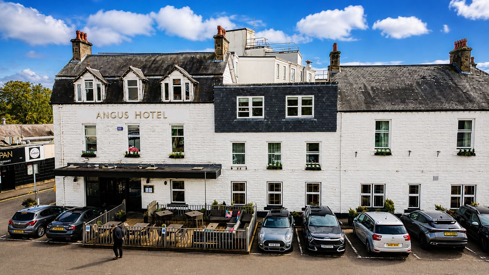 A white building with the sign 'Angus Hotel' and a parking area with several cars.
