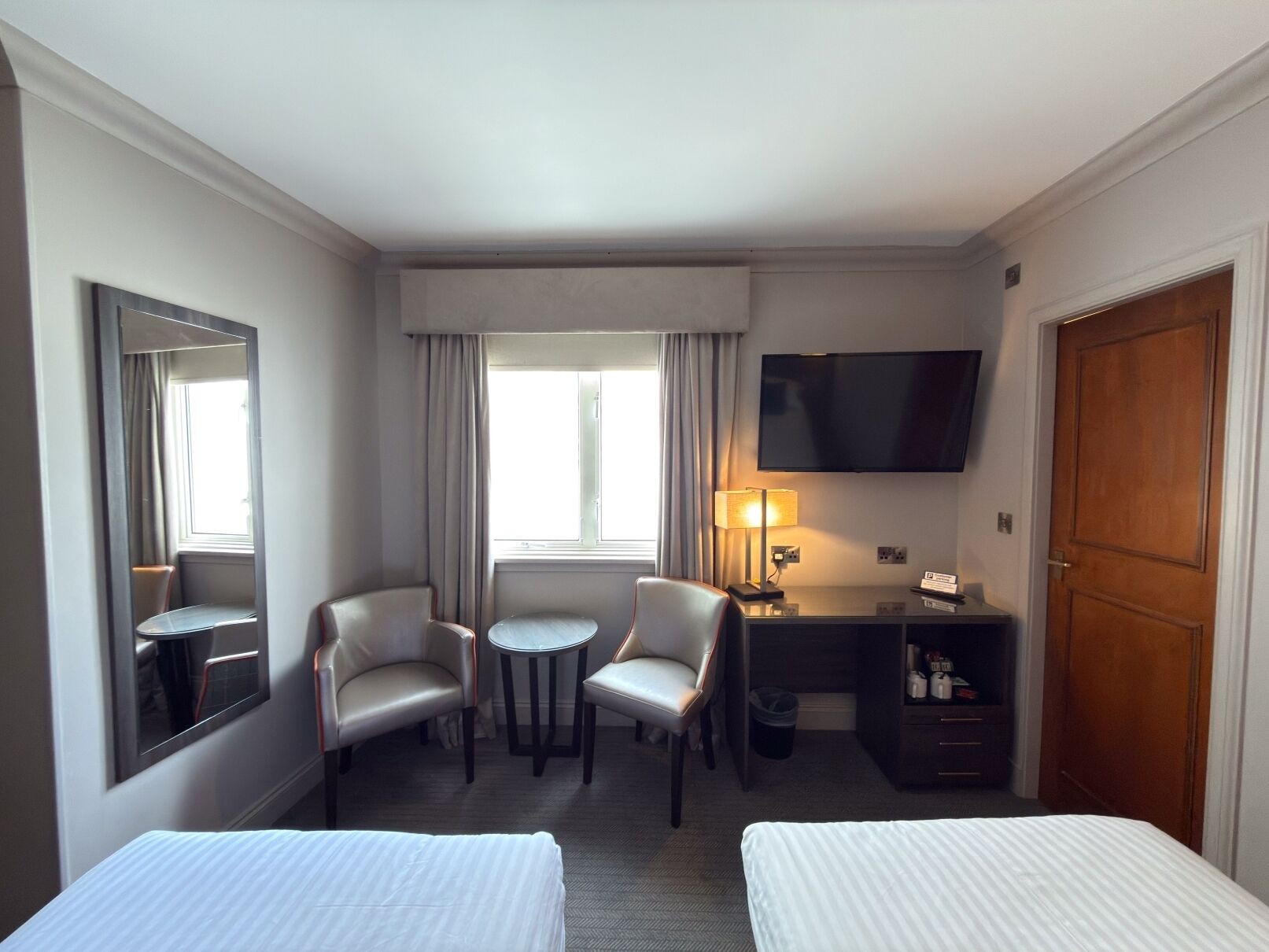 Habitación de hotel con dos camas, un escritorio, una silla, un televisor y una ventana con cortinas.