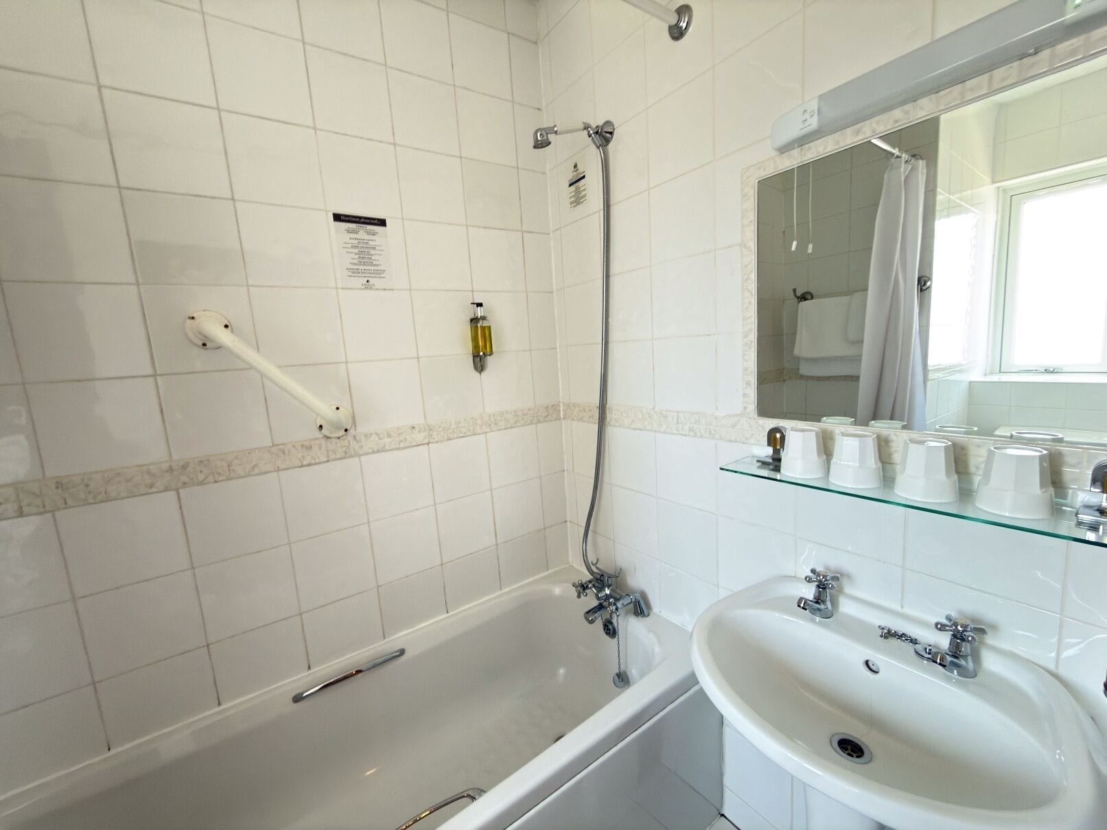 A bathroom with a bathtub, a shower, a sink, and a glass shelf with toiletries.