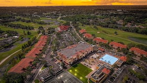 An aerial view of a residential area with a large building featuring a swimming pool, surrounded by green spaces and a golf course. - Emerald Greens Hotel Condo Resort (Tampa)