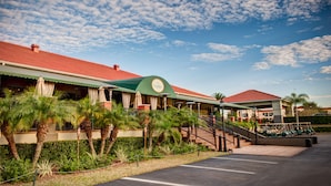 A hotel with a red roof, palm trees, and a parking lot. - Emerald Greens Hotel Condo Resort (Tampa)
