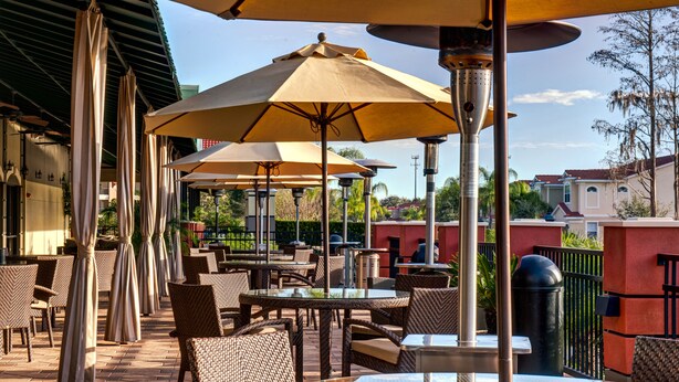 An outdoor patio area with wicker furniture, round tables, and large umbrellas providing shade. - Emerald Greens Hotel Condo Resort (Tampa)