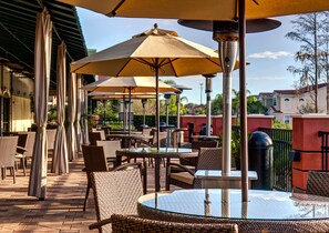 Un espace extérieur aménagé en terrasse, avec des meubles en osier, des tables rondes et de grands parasols pour créer de l’ombre.