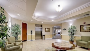 A lobby with a reception desk, a green sofa, a wooden coffee table, and potted plants. - Emerald Greens Hotel Condo Resort (Tampa)