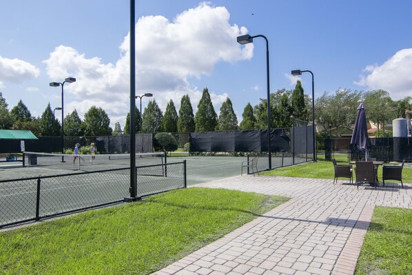 Una cancha de tenis con una cerca, sillas y una zona de estar cubierta.