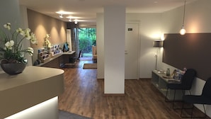 Un área de recepción moderna con suelo de madera, un mostrador de recepción, una planta en maceta y vistas al exterior.
