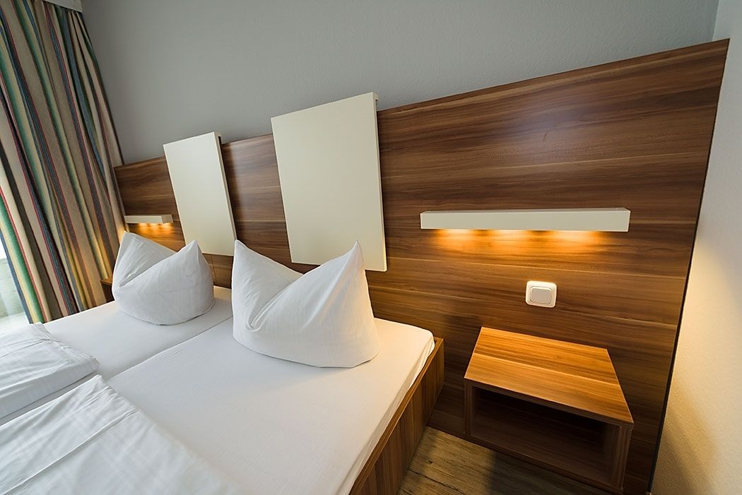 A hotel room with a wooden headboard, two white pillows, a bedside table, and a nightstand.
