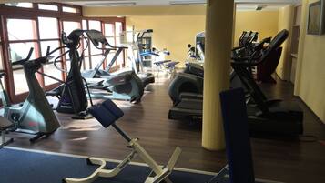 A gym with various exercise machines, including treadmills and elliptical trainers, arranged in rows.