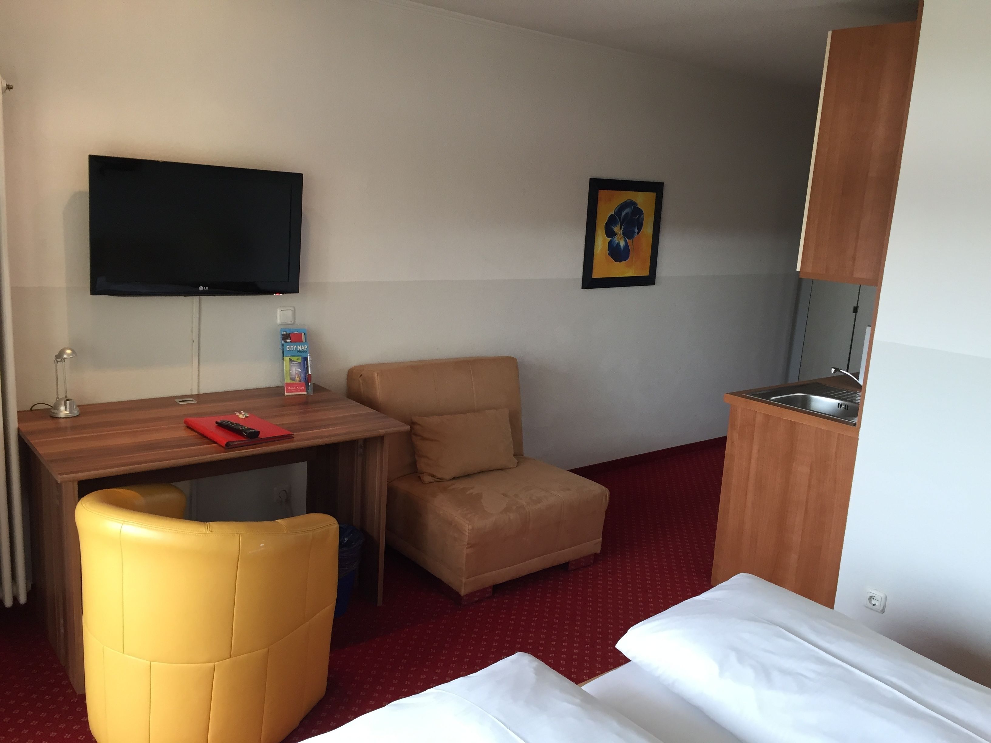 Una camera d'albergo con un letto, una scrivania con una sedia, una televisione, un angolo cottura e un quadro appeso al muro.