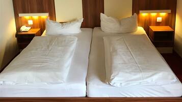 Un lit double avec du linge de lit blanc, une tête de lit en bois, deux tables de chevet avec des lampes et, au-dessus, un tableau représentant un paysage encadré.