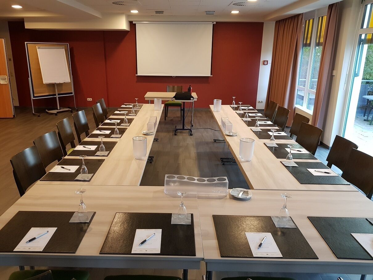 Une salle de conférence équipée d’une longue table, de chaises, d’un écran de projection et d’un tableau blanc.
