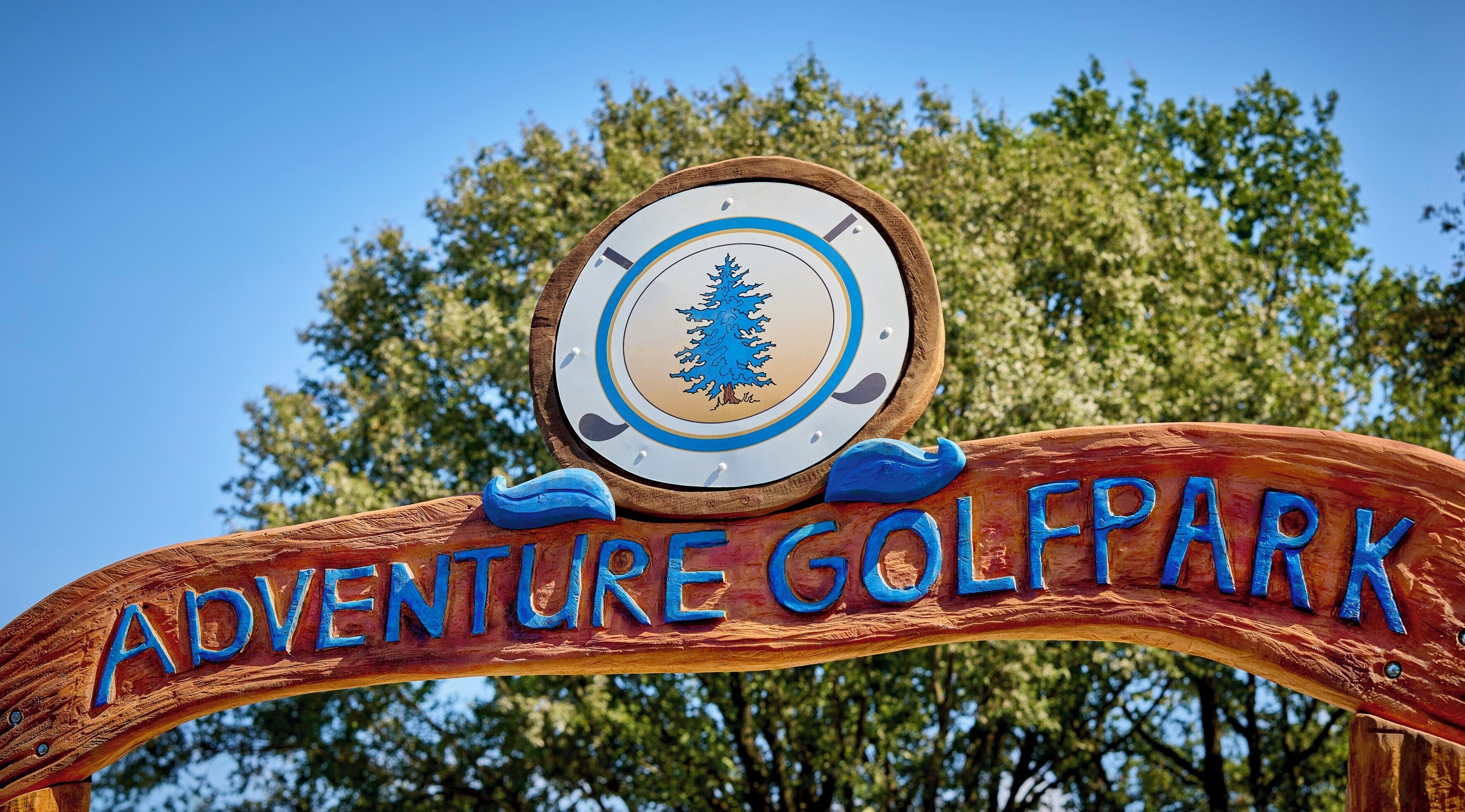 Ein hölzernes Schild mit der Aufschrift 'ADVENTURE GOLF PARK' und einem kreisförmigen Emblem mit einem Baum.