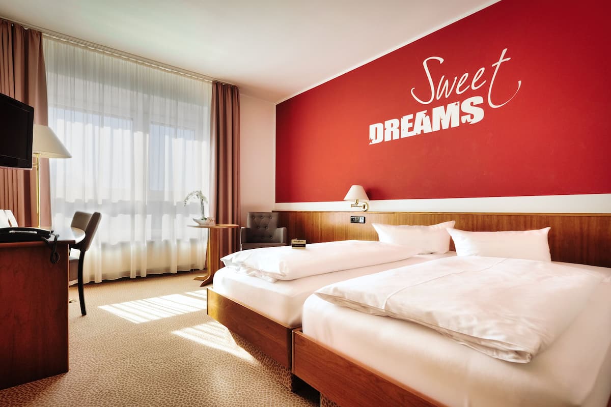 A hotel room with two beds, a desk, a chair, a TV, and a red wall with the words "Sweet Dreams".