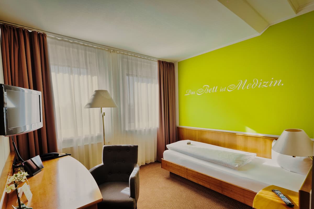 A hotel room with a bed, a desk, a chair, a TV, and a wall with a bright green color and a text.