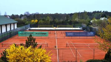 En tenniskort med reklam, omgiven av träd och en byggnad.