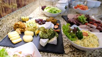 A variety of cheeses, fruits, and meats on a marble countertop.