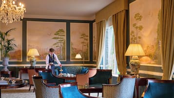 Ein formeller Speisesaal mit einem Kellner, eleganten Stühlen, einem für eine Mahlzeit gedeckten Tisch und einem großen Fenster mit Vorhängen.