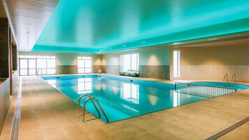 Une piscine intérieure à l’eau claire, dotée d’un sol carrelé et d’un design de plafond moderne.