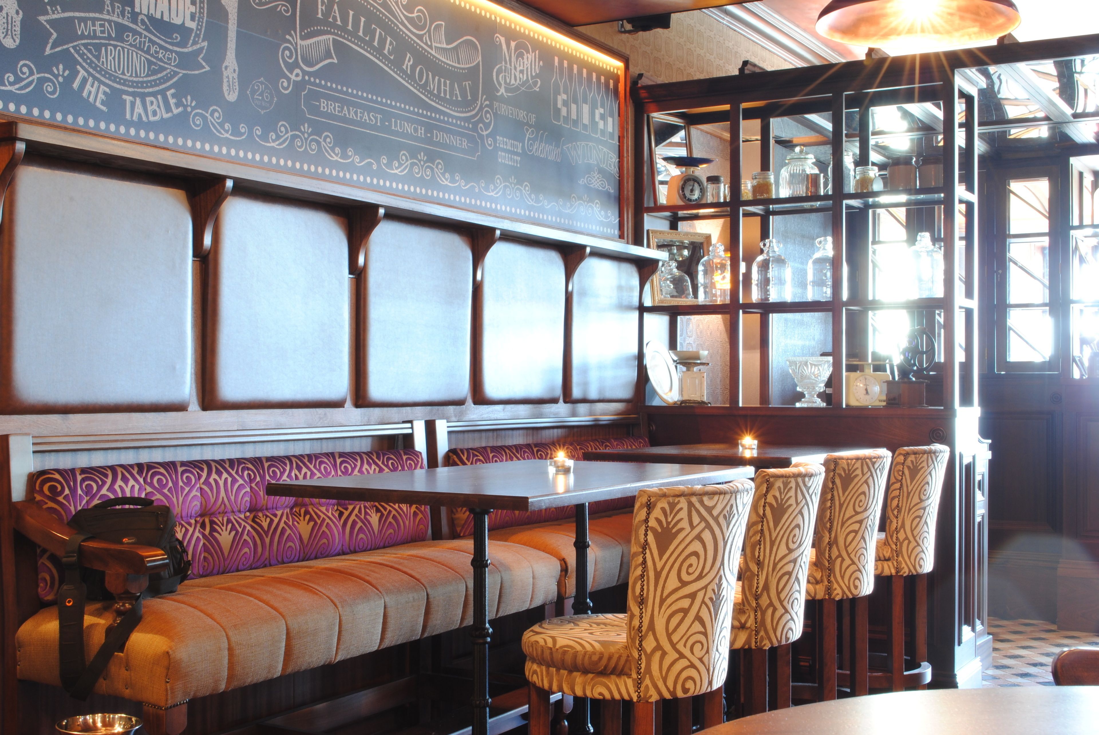 A restaurant with a long bench seating area, a bar with stools, and a display case with glassware.
