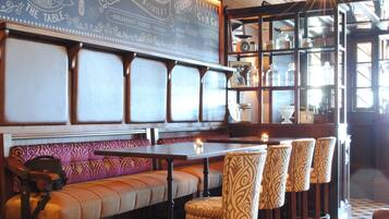 A restaurant with a long bench seating area, a bar with stools, and a display case with glassware.